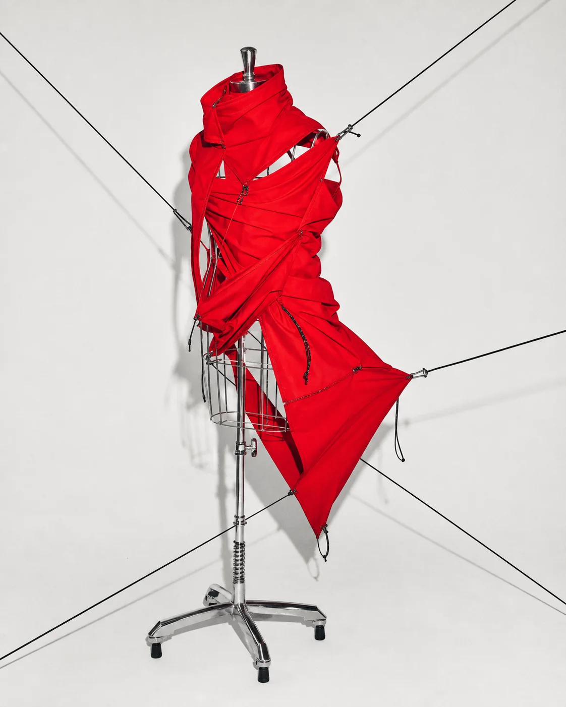Sculptural red garment on a chrome dress form in the hided studio aesthetic